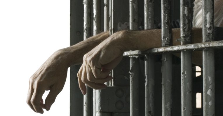 hands dangling through prison bars